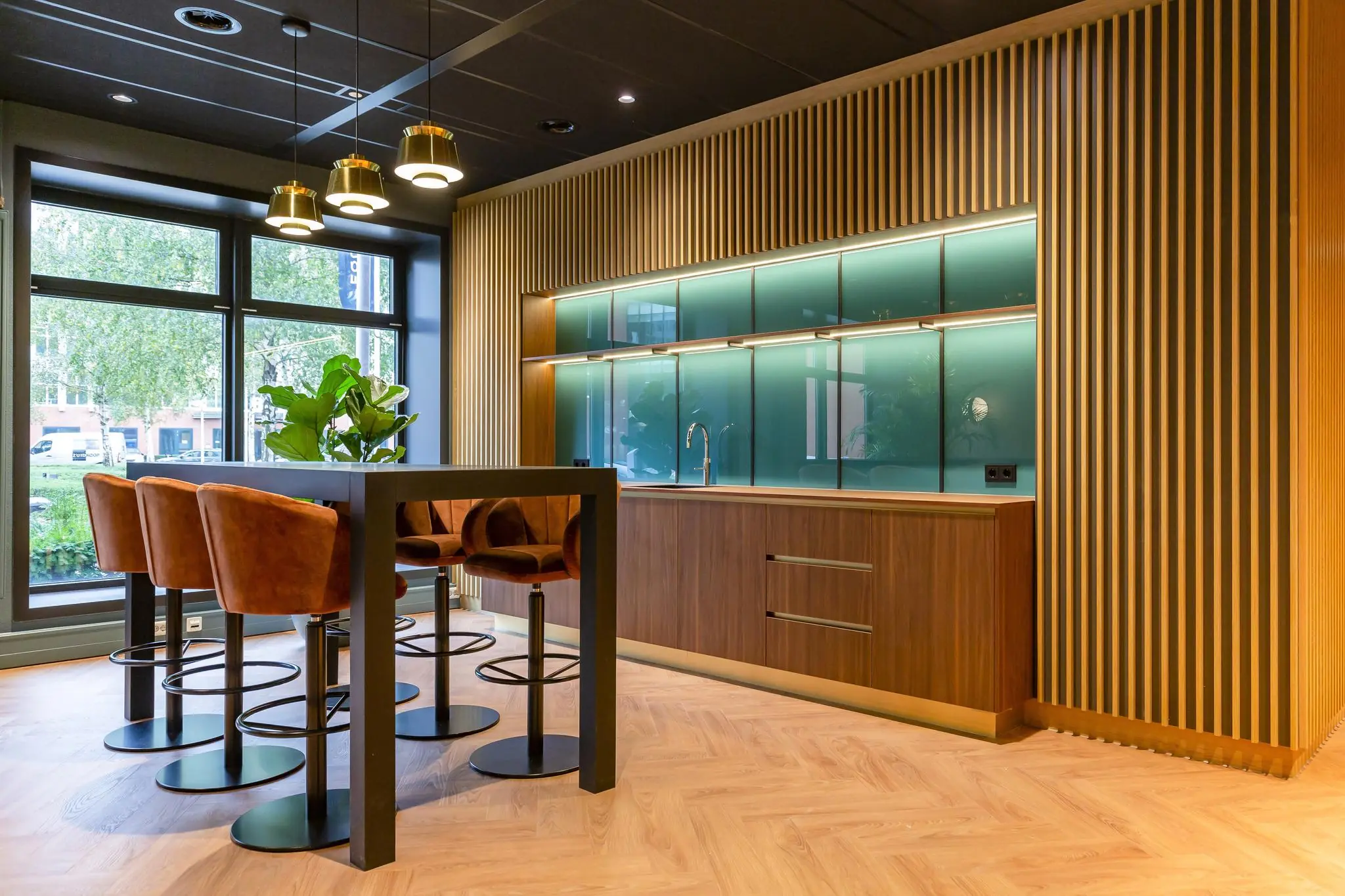 Moderne kantoorkeuken aan de George Hintzenweg met houten afwerking, hoge zitstoelen en groene glazen achterwand.